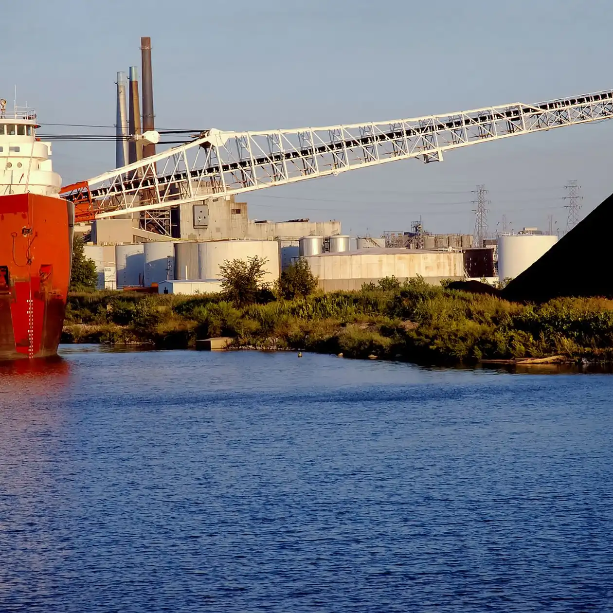 A bulk carrier at an industrial berth beside a dark coal pile and conveyor