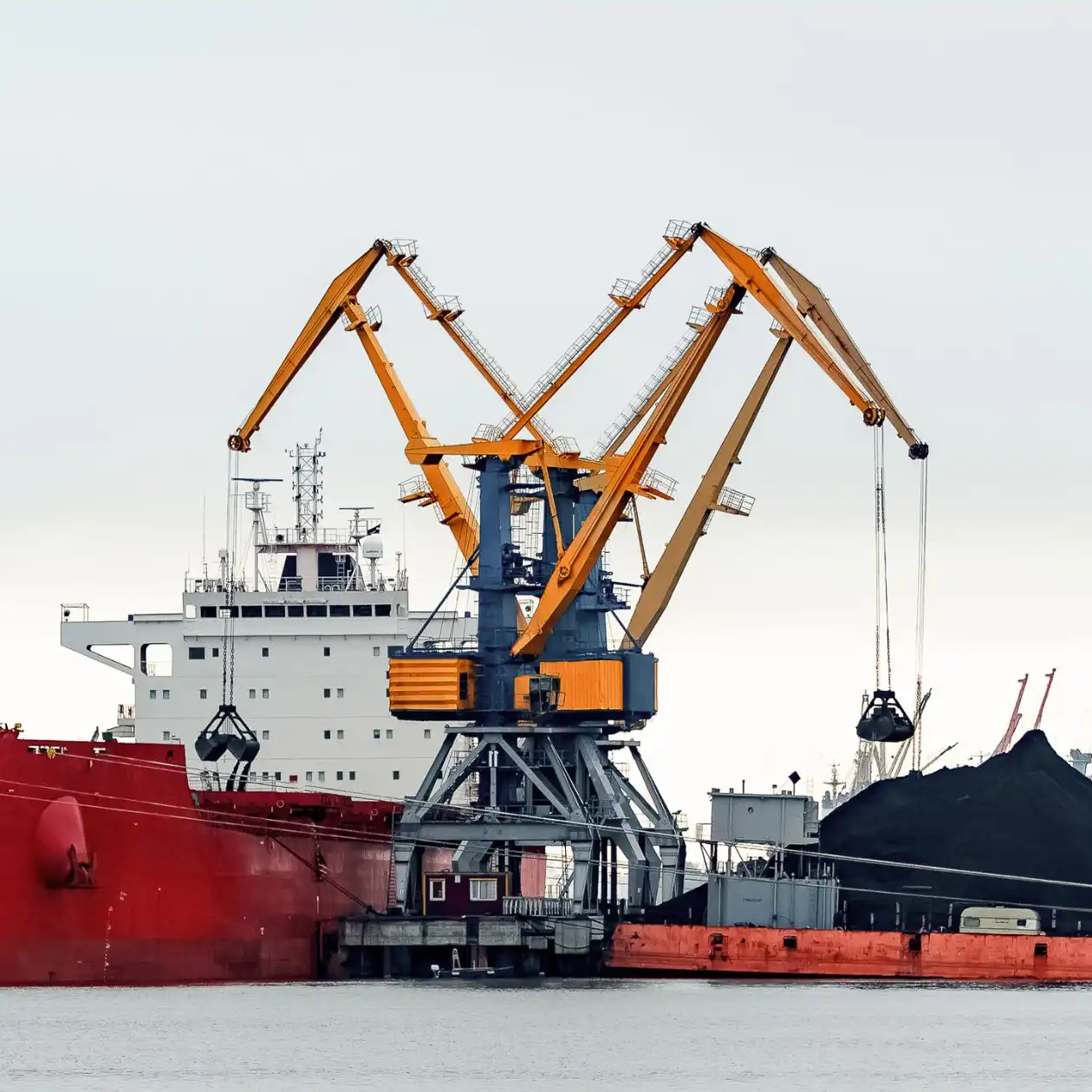 A red bulk carrier with yellow cranes handling thermal coal at a port